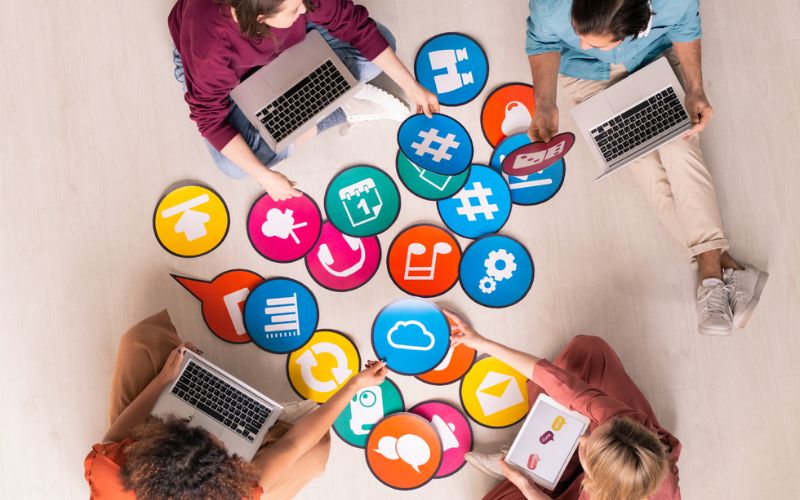 Four people working on laptops at a table, surrounded by social media icons.