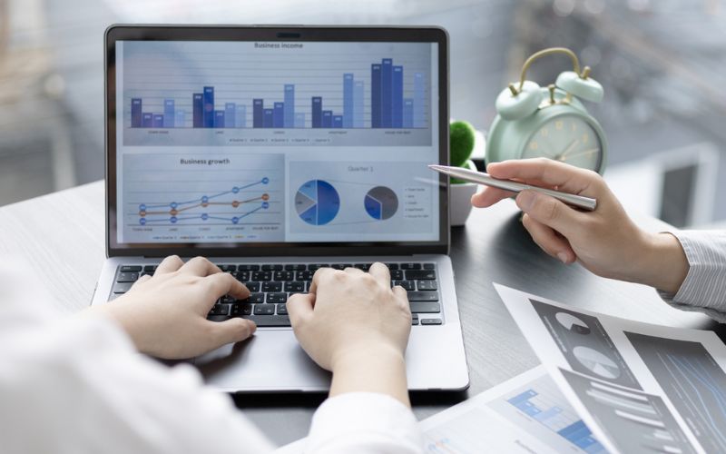 Business professionals analyzing data on laptop screen with graphs and charts.